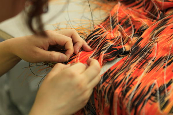 工作人员正在手工将一种玻璃丝编织到服装上